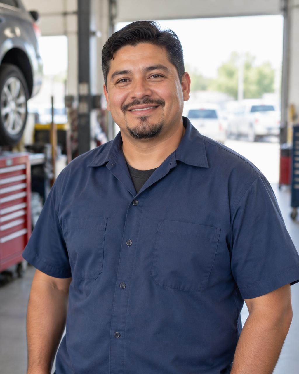 Technician in a blue work shirt smiling in a daylit bay at Carmen's Foreign Car Repair in Cranford, New Jersey